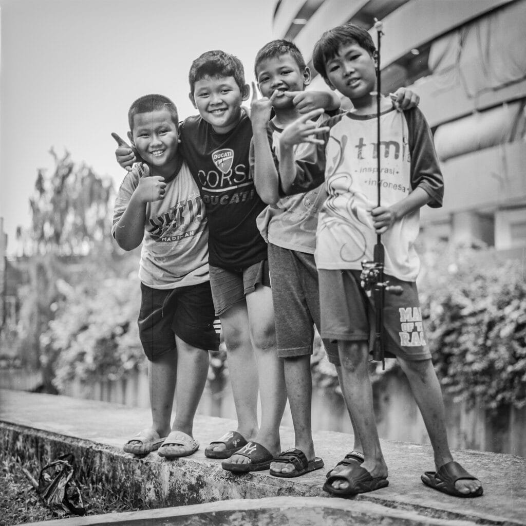 Groupe de jeunes garçons posant joyeusement au bord d’un canal à Jakarta, avec une canne à pêche.