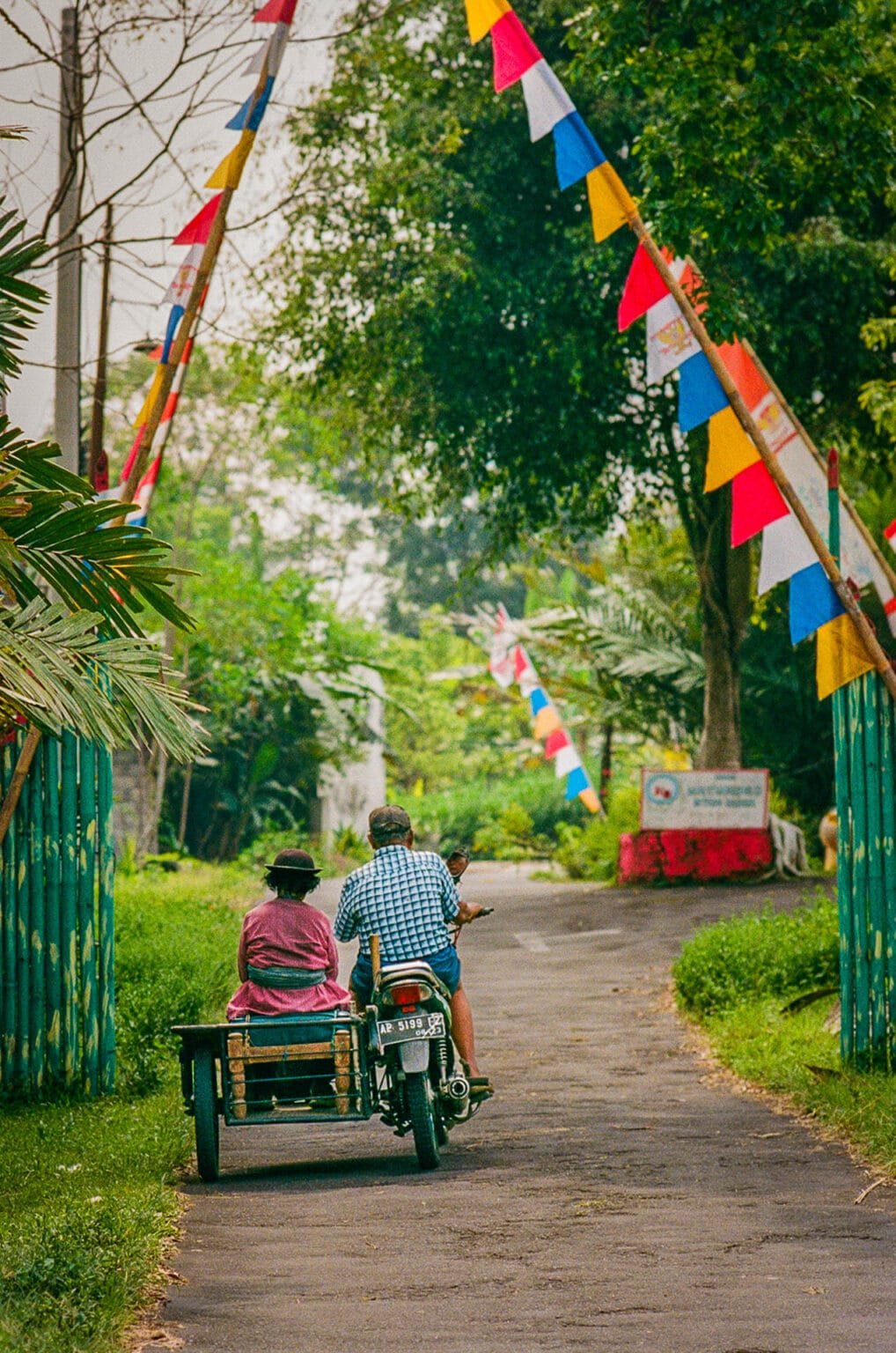Couple à moto avec side-car sur une route de campagne décorée de fanions en Indonésie.