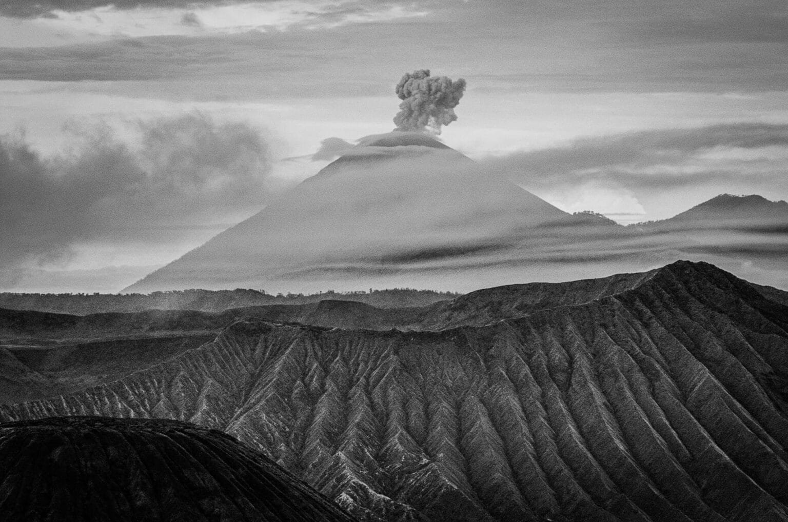 Vue en noir et blanc du Mont Bromo depuis King Kong Hill, avec le Semeru en arrière-plan en éruption.