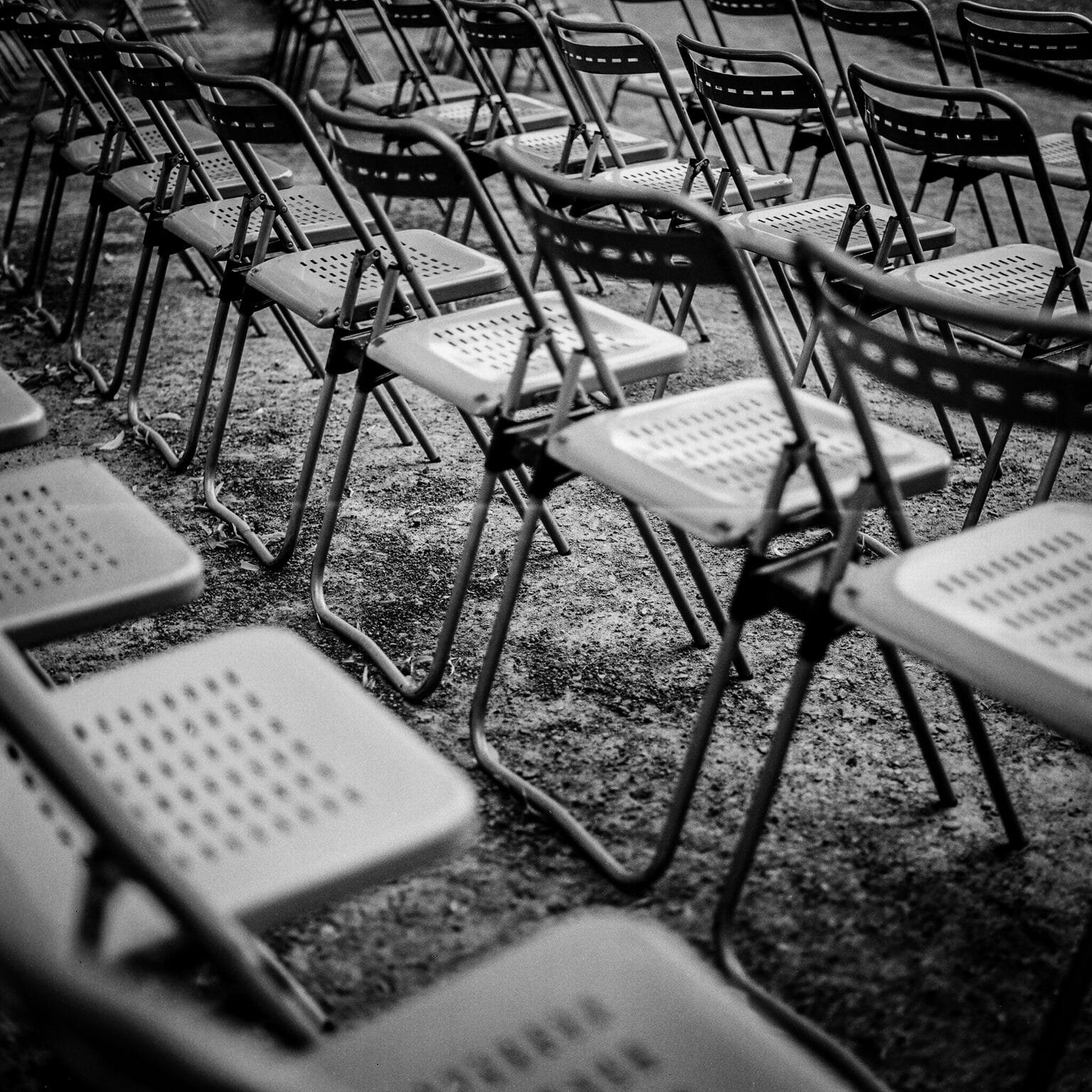 Rangées de chaises vides en métal au Jardin des plantes de Nantes, photographiées en noir et blanc avec un Hasselblad.