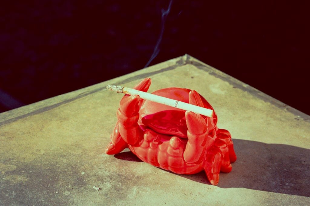 Cendrier en forme de crabe rouge tenant une cigarette allumée sur une table de balcon