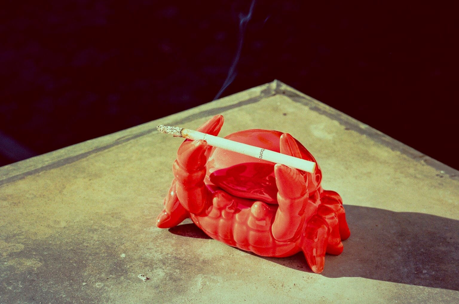 Cendrier en forme de crabe rouge tenant une cigarette allumée sur une table de balcon