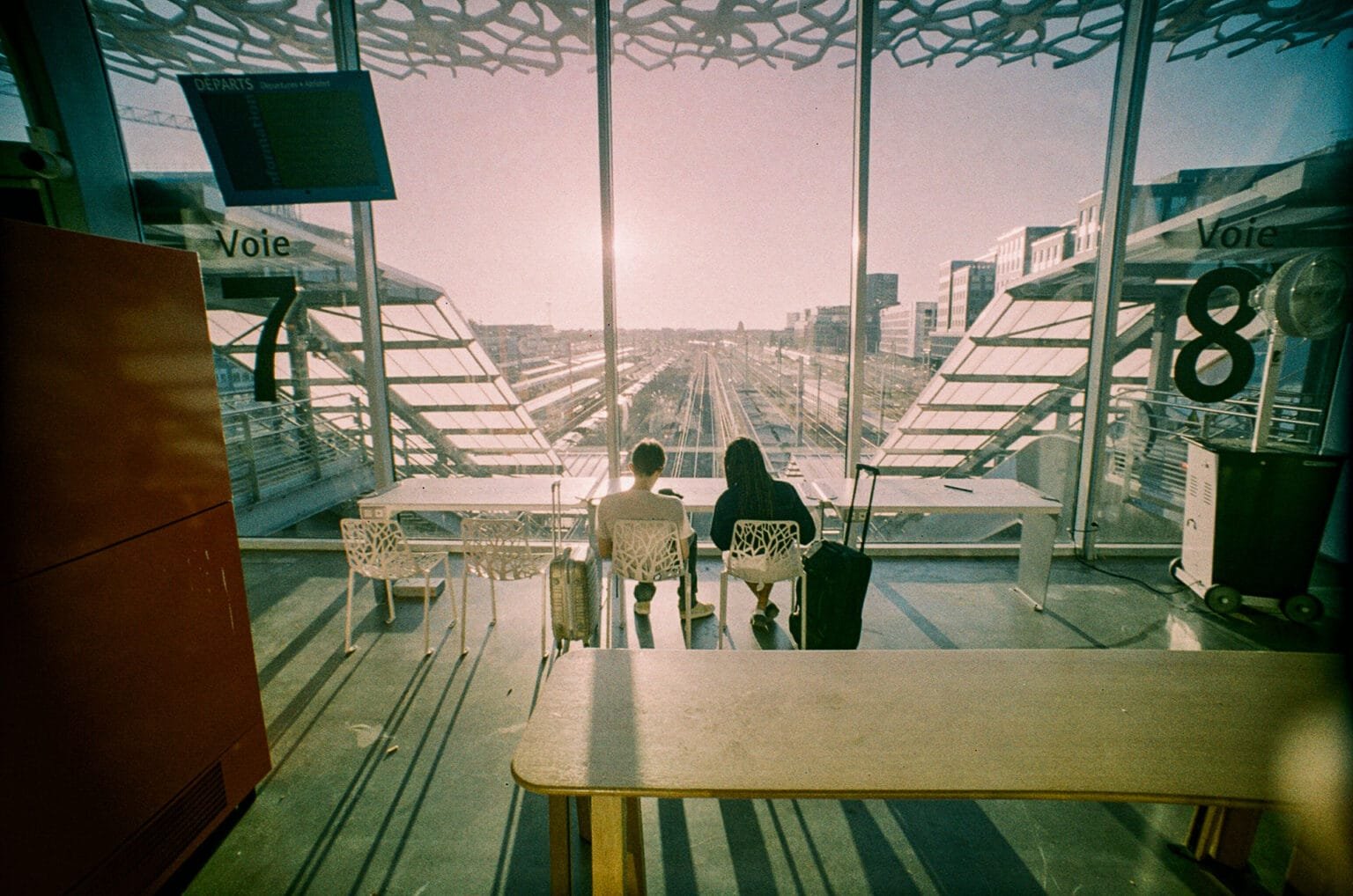 Deux voyageurs assis face aux voies ferrées à la gare de Nantes, photographiés avec un Lomo LC-Wide sur pellicule Retropolis.