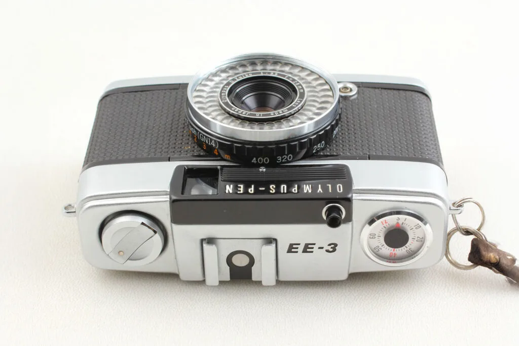 Vue de dessus de l’Olympus Pen EE-3 avec molette de rembobinage, sabot porte-accessoire et bague de sensibilité ASA.