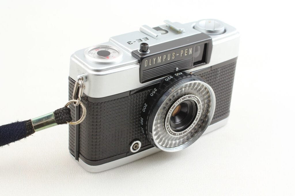 Olympus Pen EE-3 vu de trois-quarts avec sa dragonne, montrant le déclencheur et la bague ASA.