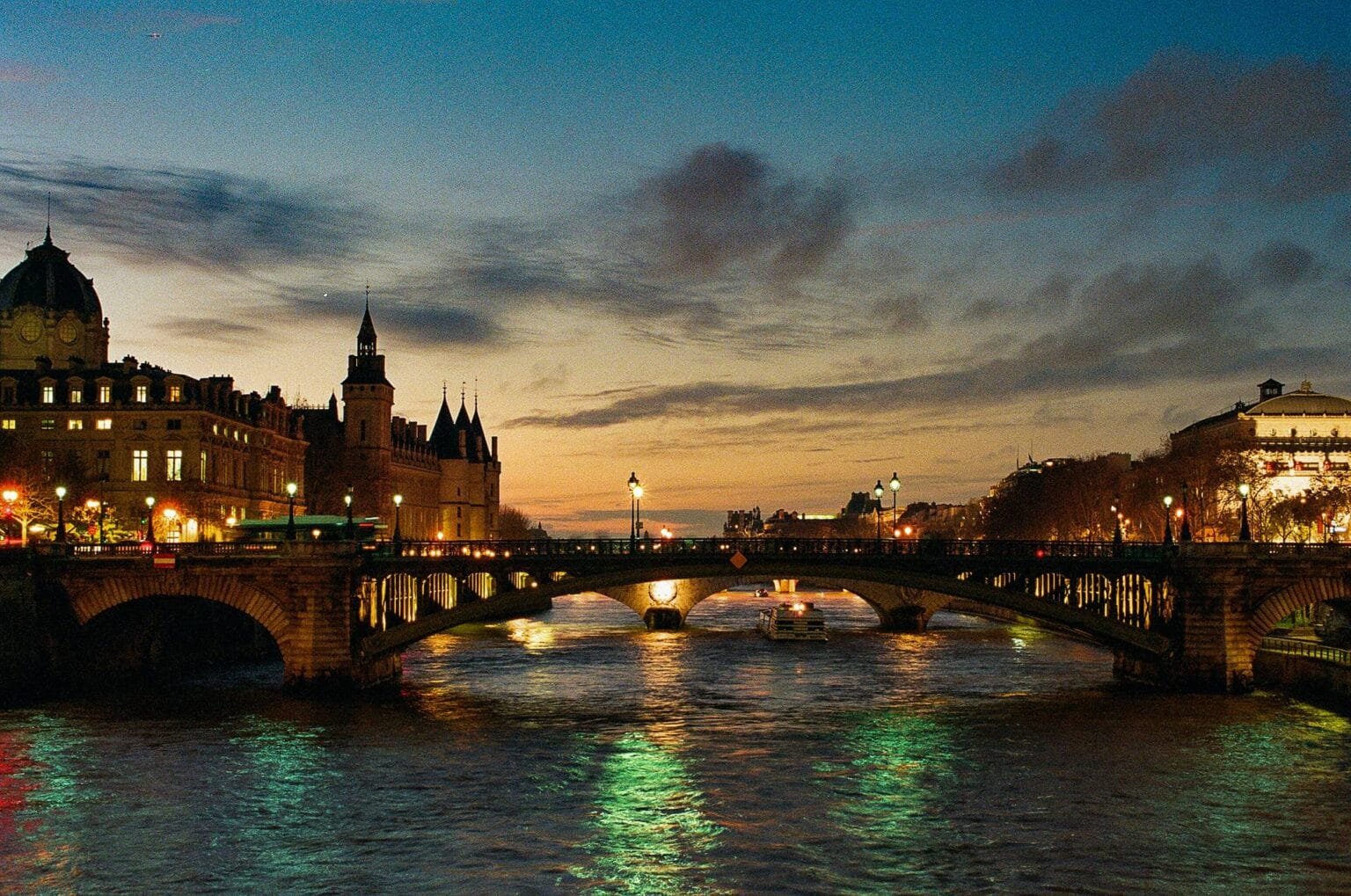Vue du pont au cœur de Paris à l’heure bleue, avec la Conciergerie et les reflets des lumières sur la Seine