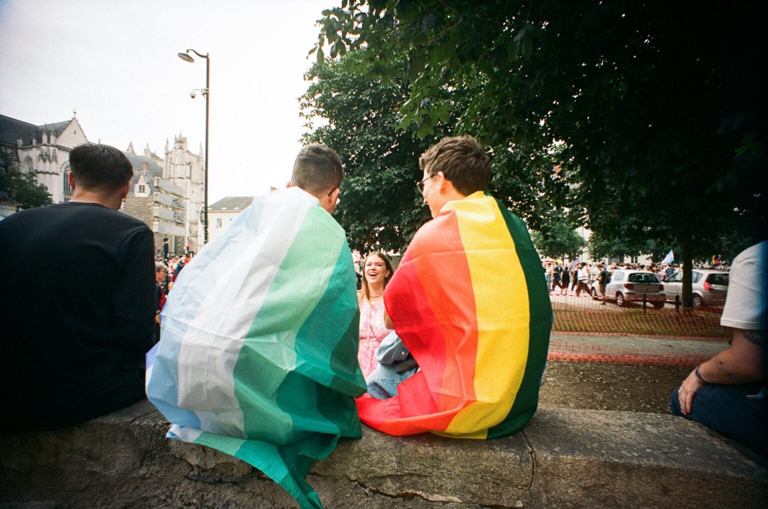 eux personnes assises portant des drapeaux LGBTQIA+ en cape, lors de la Pride de Nantes.