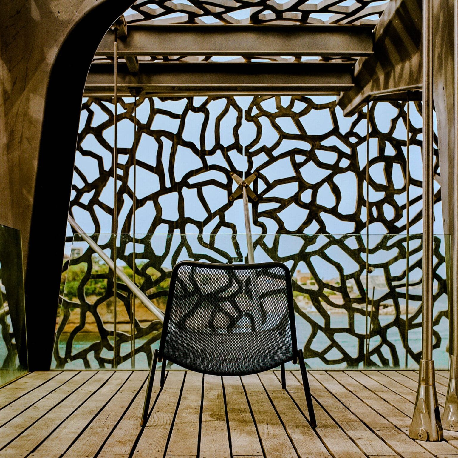 Fauteuil vide sur une terrasse en bois face à la façade ajourée du Mucem à Marseille, photographié avec un Hasselblad 500 C/M et une pellicule Kodak Gold 200.