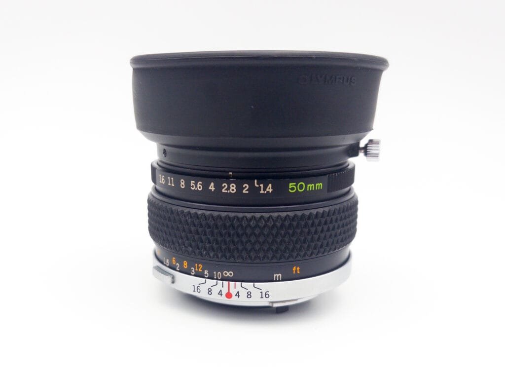 Objectif Olympus Zuiko 50mm f/1.4 vu de côté, avec pare-soleil en caoutchouc déplié.