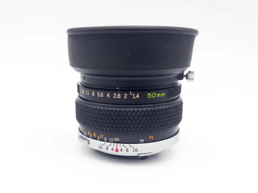 Objectif Olympus Zuiko 50mm f/1.4 vu de côté, avec pare-soleil en caoutchouc déplié.