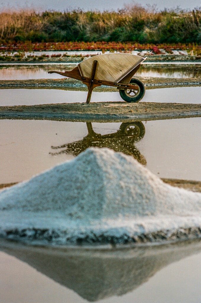 Tas de sel et brouette traditionnelle dans les marais salants de Guérande, avec reflets dans l’eau.