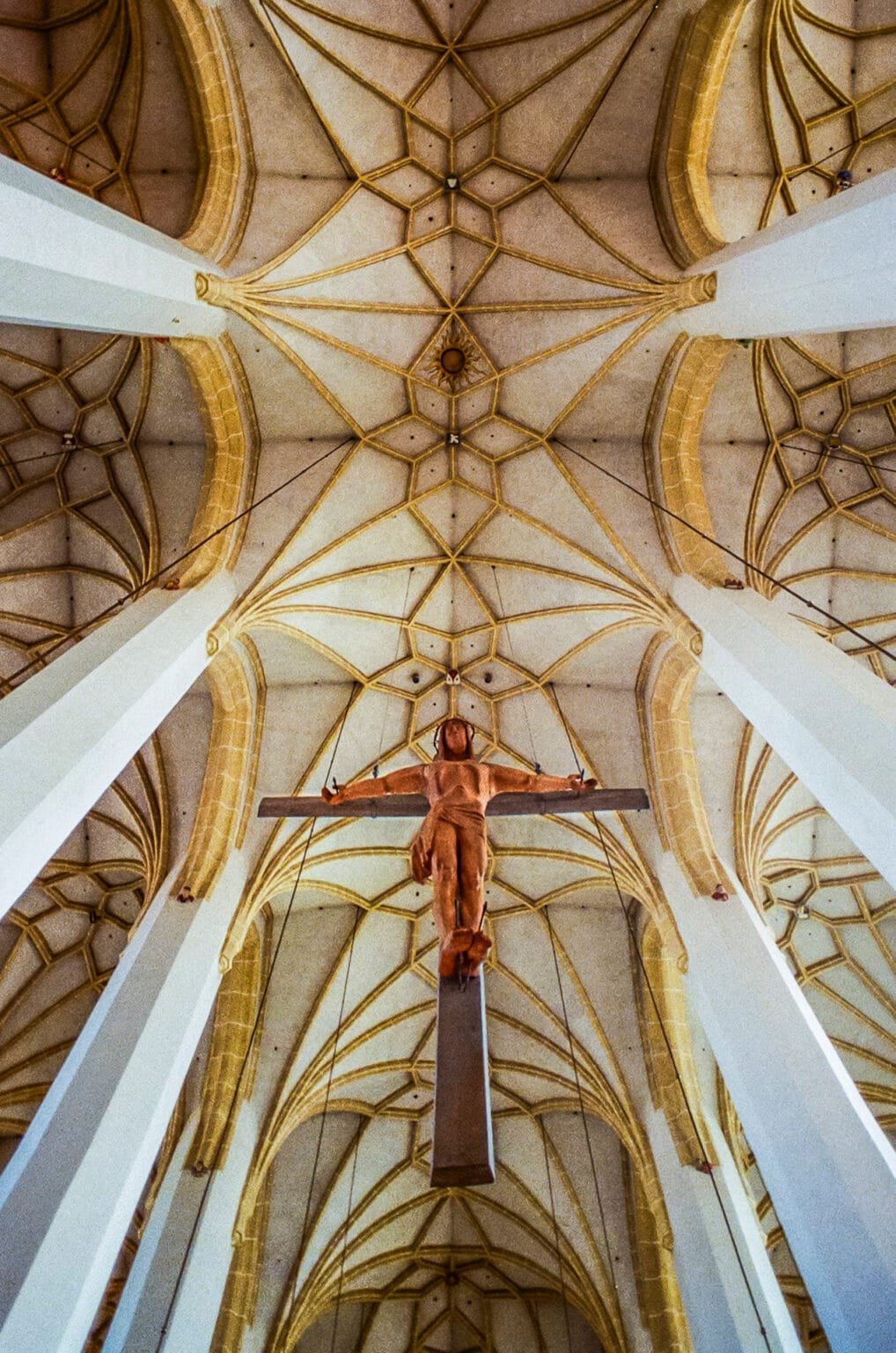 Voûte gothique de la cathédrale de Munich avec un Christ suspendu au centre, vue en contre-plongée.