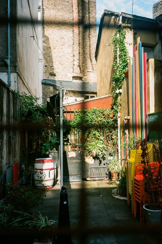 Petite cour intérieure colorée à Nantes, avec des chaises empilées, des plantes et un tonneau, photographiée avec un Olympus AF-1 sur pellicule Portra 160.