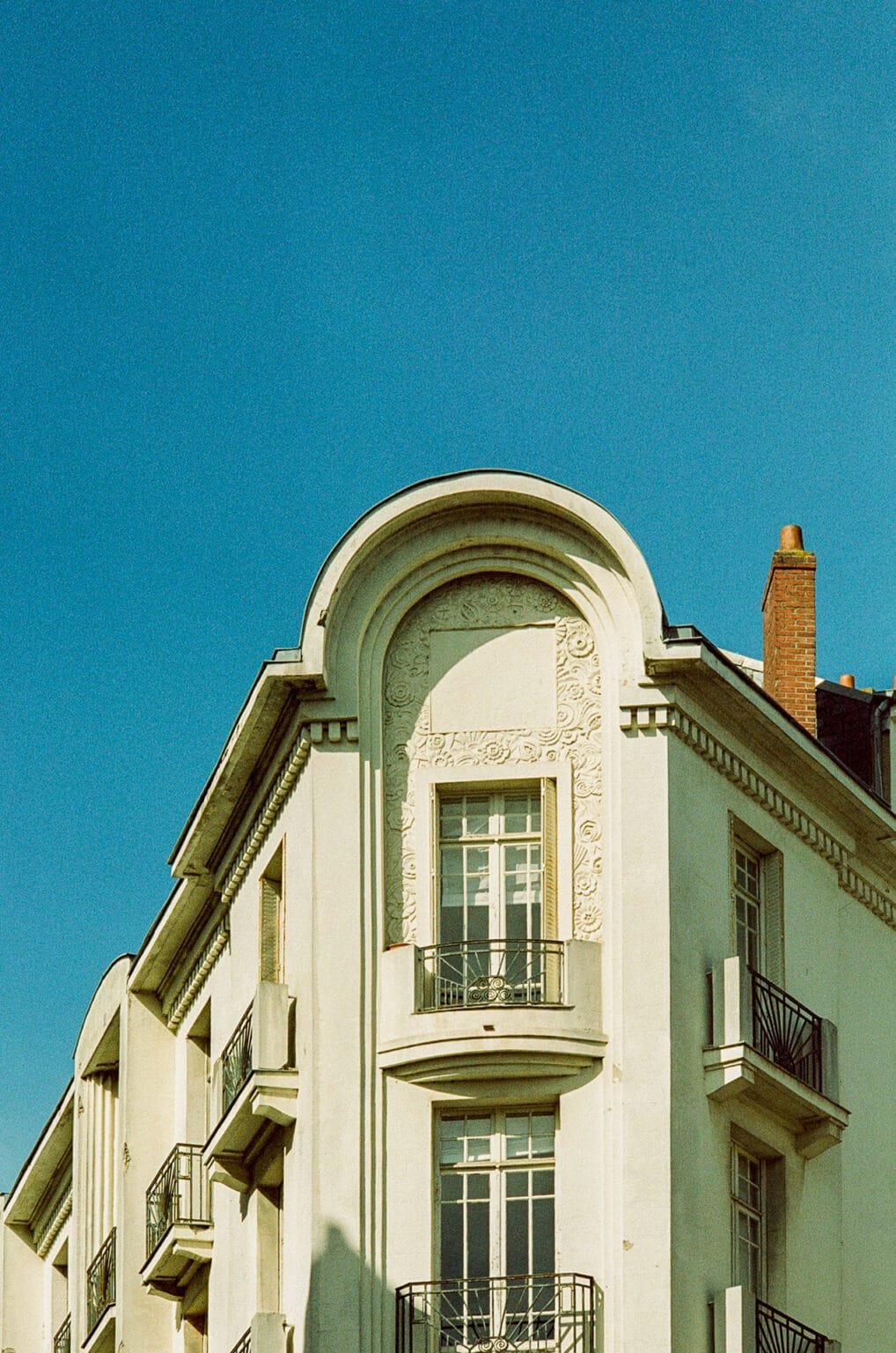 Façade blanche d’un immeuble art déco à Nantes, ornée de motifs floraux et surmontée d’un fronton arrondi.