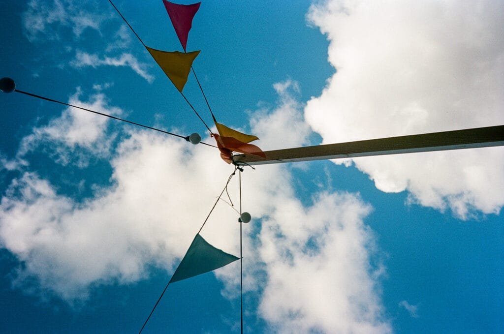Fanions colorés photographiés en contre-plongée dans un ciel bleu parsemé de nuages à Nantes avec un Olympus AF-1 et une pellicule Kodak Portra 160.