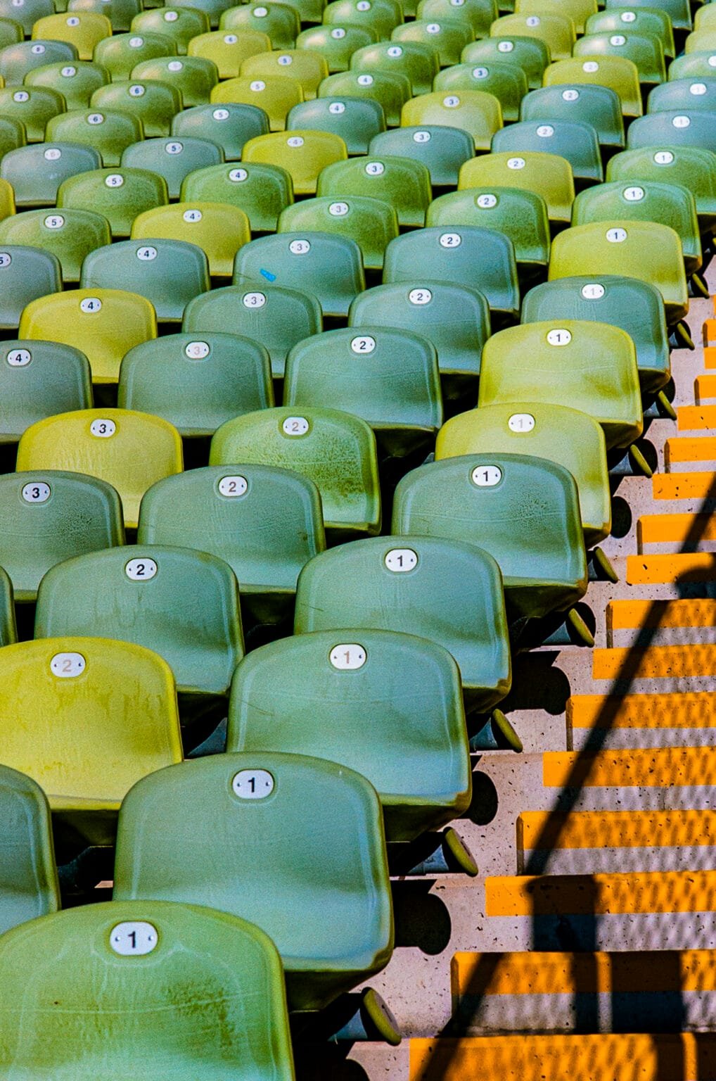 Alignement de sièges verts numérotés dans les gradins du Stade Olympique de Munich, éclairés par la lumière du matin.