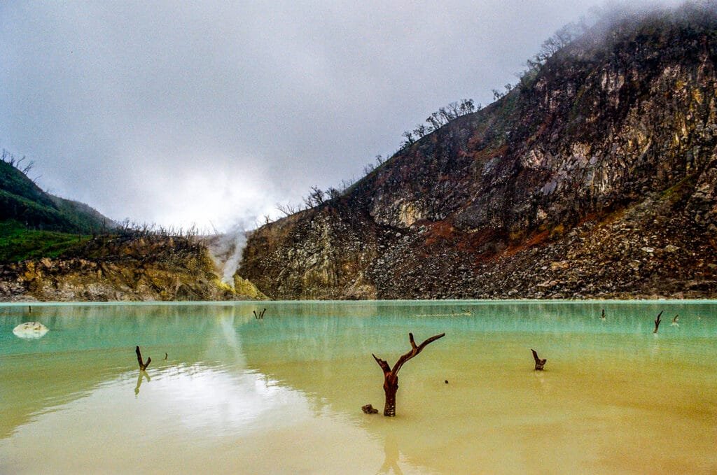 Lac de soufre aux eaux turquoise à Kawah Putih, près de Ciwidey, avec des troncs d’arbres émergents, photographié sur pellicule Portra 160.