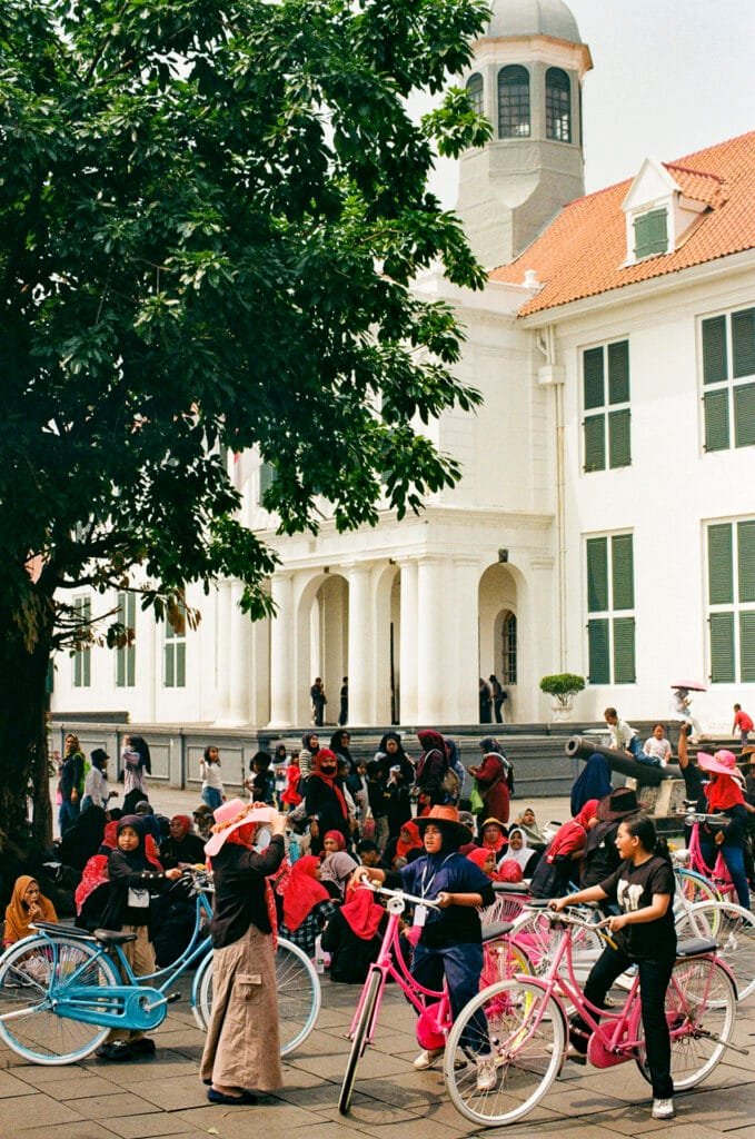 Enfants et visiteurs autour de vélos colorés à Kota Tua, devant un bâtiment colonial blanc à Jakarta.