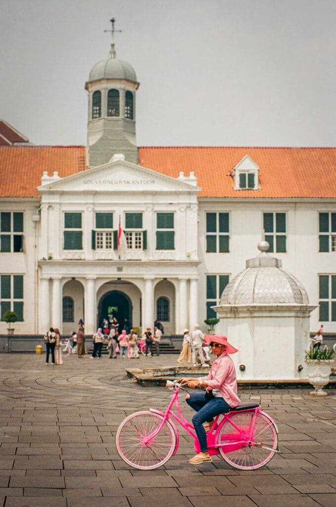 Femme en rose sur un vélo rose devant le musée d’Histoire de Jakarta à Kota Tua.
