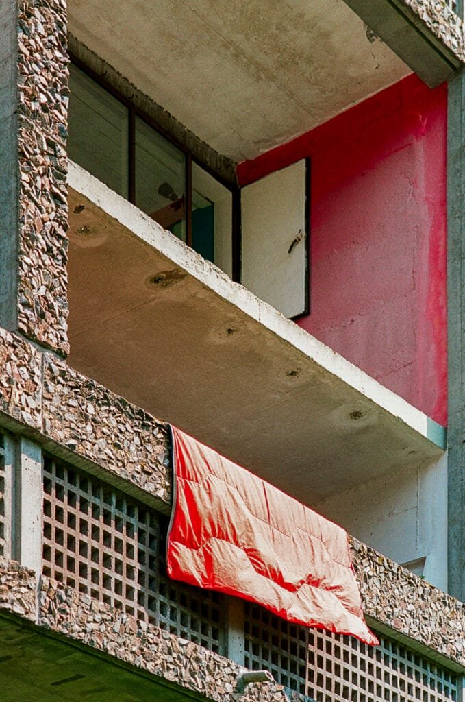 Couette rouge suspendue à un balcon en béton brut de la Maison Radieuse de Rezé, photographiée en argentique avec un Nikon F3 HP.
