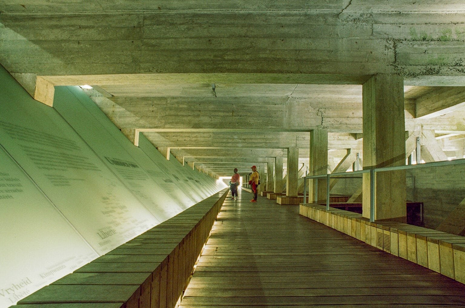 Passage souterrain en béton du Mémorial de l’abolition de l’esclavage à Nantes, photographié en grand angle avec deux visiteurs au fond de la perspective.