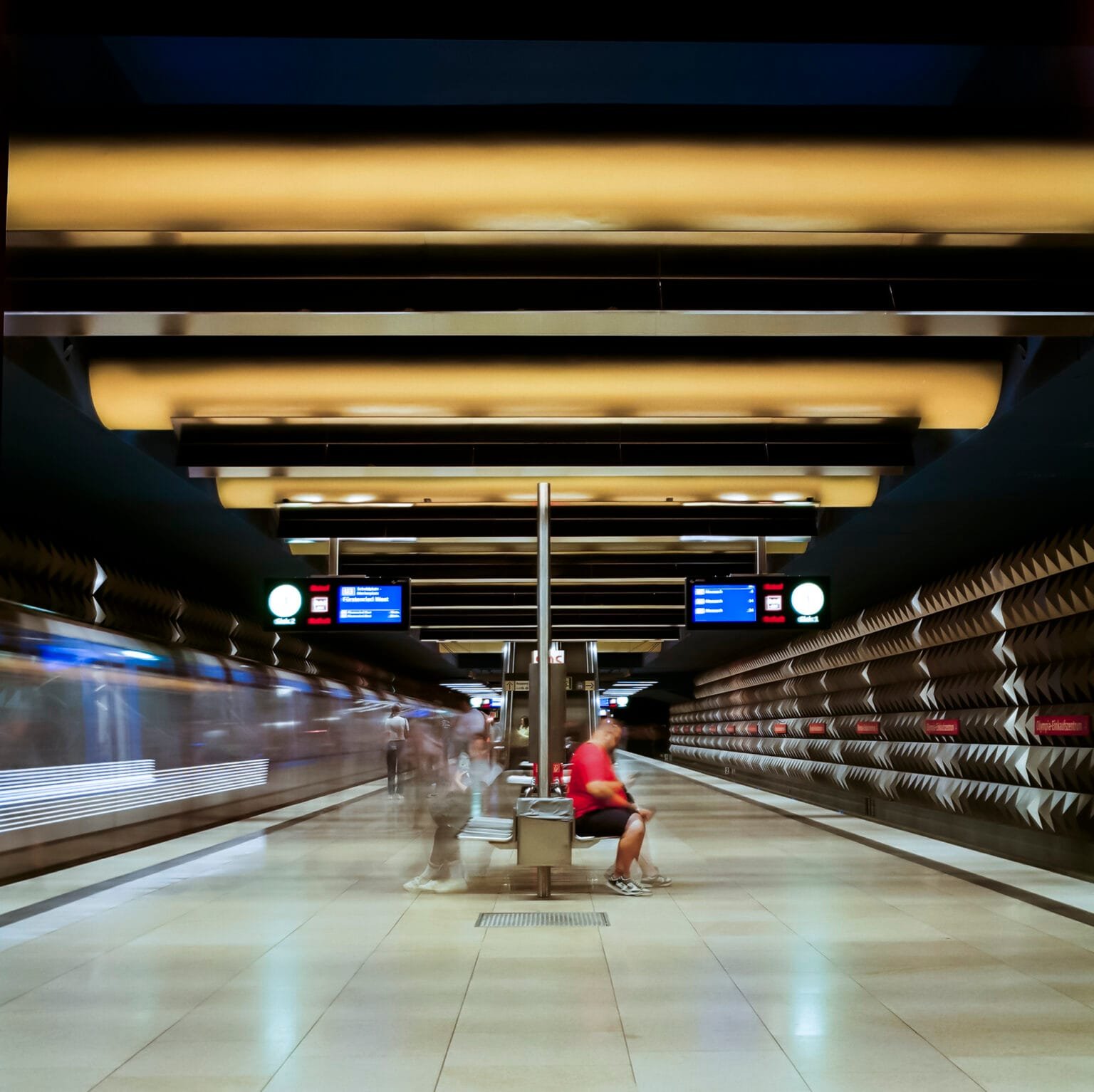 Station de métro Olympia-Einkaufszentrum à Munich, photographiée en pose longue avec un passager immobile au centre.
