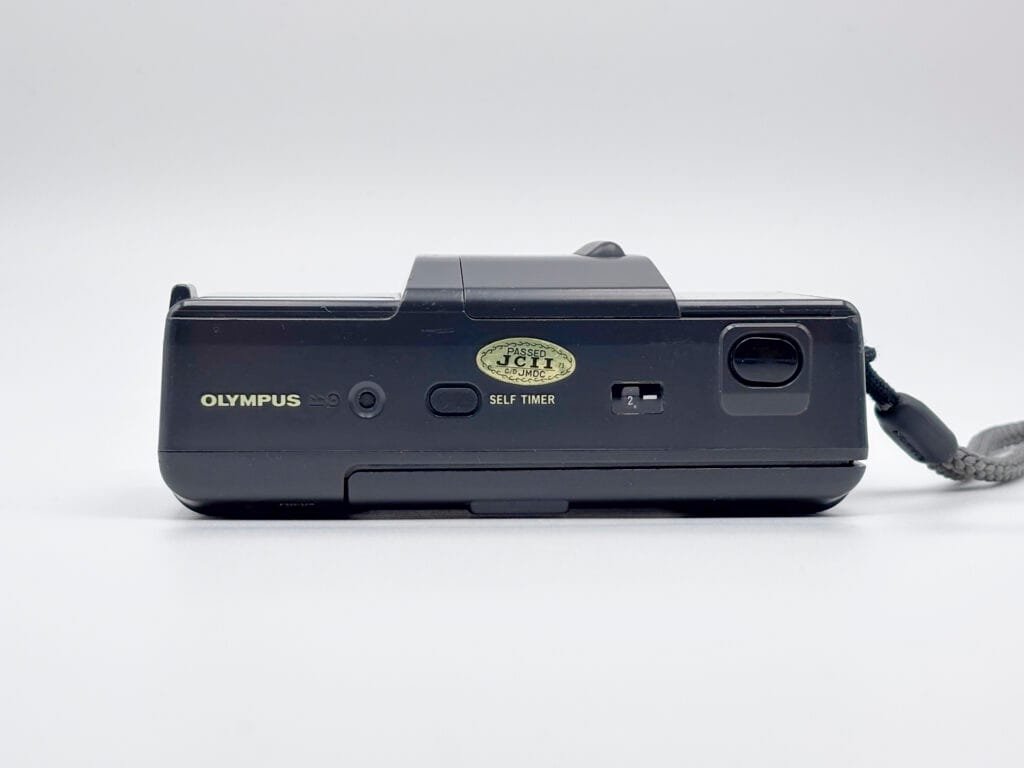Vue du dessus de l’Olympus AF-1 avec bouton du retardateur et sticker JCII doré.