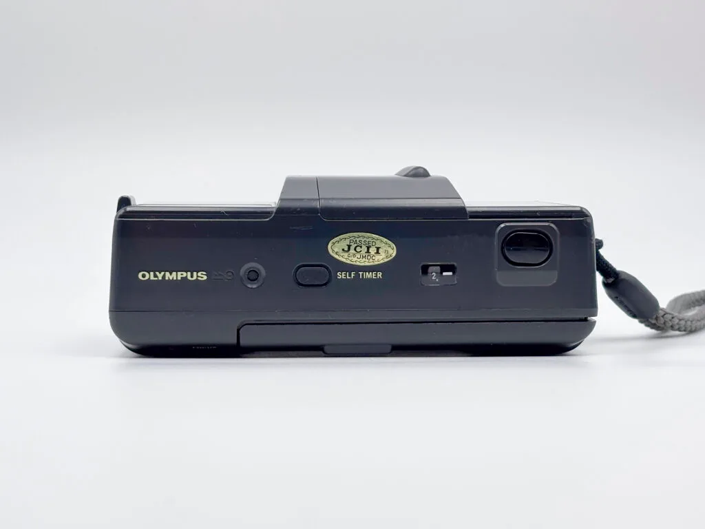 Vue du dessus de l’Olympus AF-1 avec bouton du retardateur et sticker JCII doré.