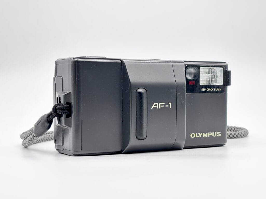Olympus AF-1 vu de trois-quarts, compact autofocus argentique avec flash intégré.