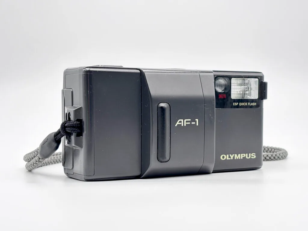 Olympus AF-1 vu de trois-quarts, compact autofocus argentique avec flash intégré.