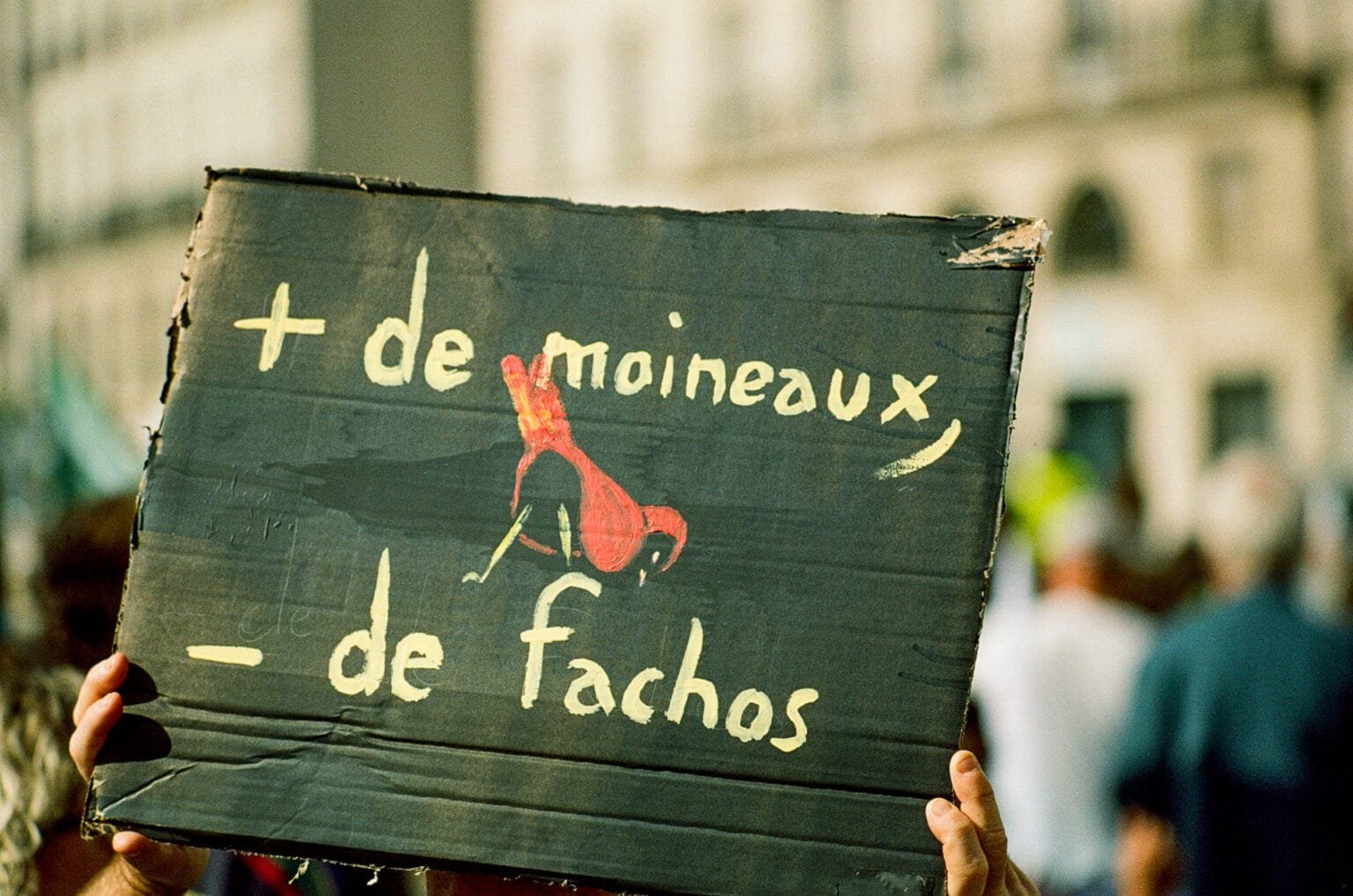Pancarte en carton tenue lors d’une manifestation à Nantes, portant l’inscription “+ de moineaux – de fachos” avec un oiseau peint en rouge, photographiée en argentique.