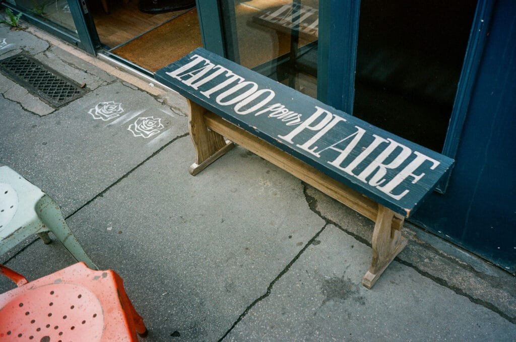 Banc en bois peint devant une boutique à Nantes, portant l’inscription “Tattoo pour plaire”, photographié avec un Olympus AF-1 sur pellicule Portra 160.