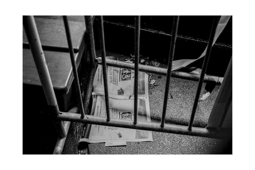 Affiche “ascenseur hors service” coincée derrière une barrière métallique au parking Gare Nord de Nantes, photographiée en noir et blanc.