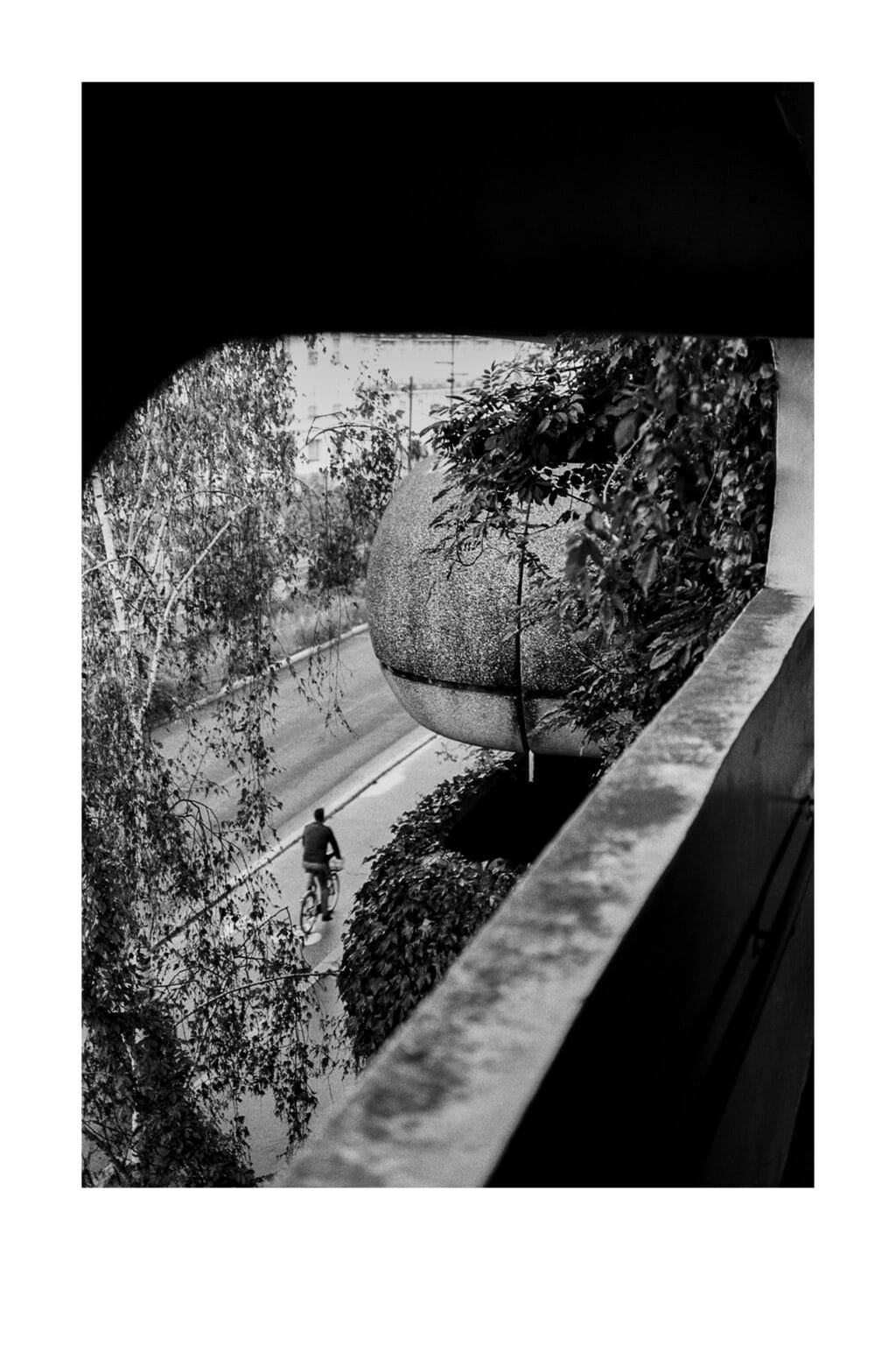 Cycliste passant au pied du parking Gare Nord de Nantes, vu depuis un étage supérieur, photographié en noir et blanc.
