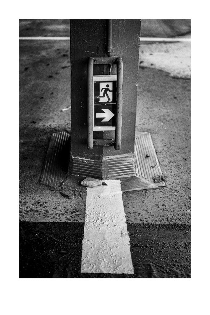 Panneau de sortie de secours fixé à un poteau du parking Gare Nord de Nantes, photographié en noir et blanc avec un Nikon F3 HP.