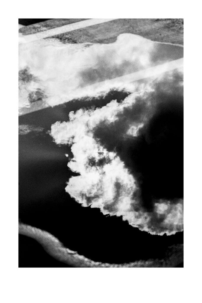 Reflet de nuages dans une flaque d’eau sur le sol du parking Gare Nord de Nantes, photographié en noir et blanc.