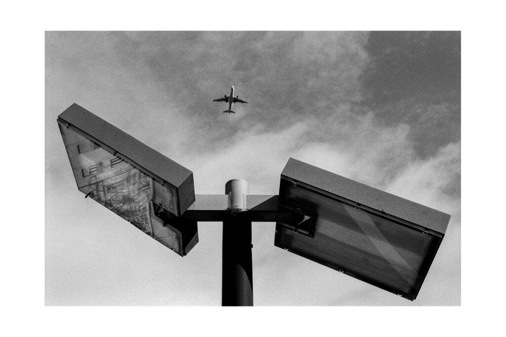 Avion dans le ciel au-dessus d’un lampadaire métallique du parking Gare Nord de Nantes, photographié en noir et blanc avec un Nikon F3 HP.