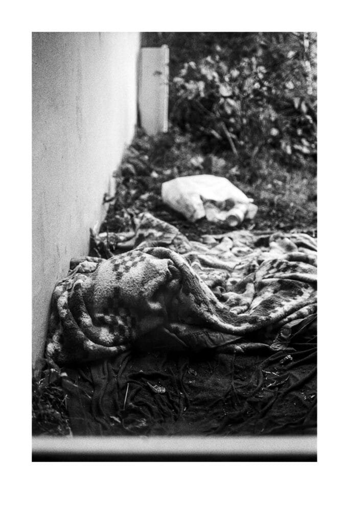 Lit de fortune contre un mur, couvertures abandonnées près du parking Gare Nord de Nantes, en noir et blanc.