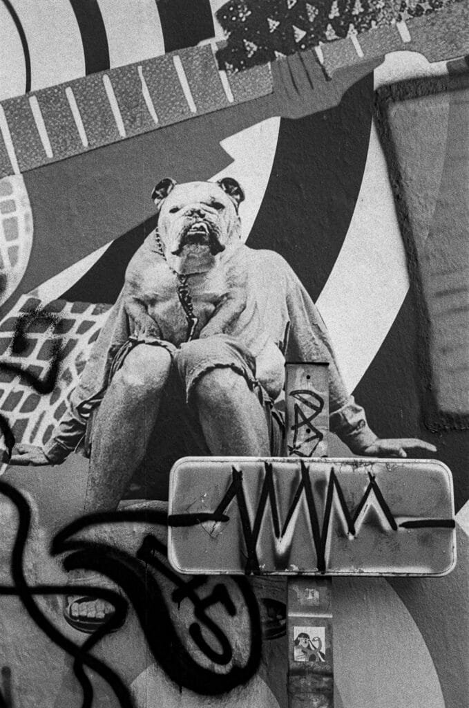 Collage mural à Nantes inspiré d’une célèbre photo d’Eliot Erwitt montrant un homme au torse nu avec une tête de bouledogue, sur fond de graffitis et de panneau détourné.