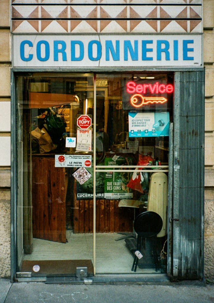 Devanture d’une cordonnerie parisienne avec enseigne bleue et néon “Service”, photographiée sur pellicule Portra 160 avec un Canon Dial 35-2