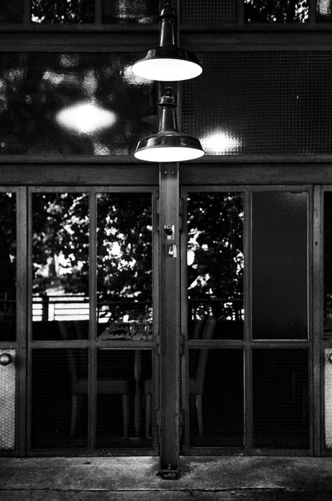 Vue centrée sur l’entrée du Lieu Unique à Nantes, avec deux lampes suspendues éclairant une façade vitrée dans une ambiance nocturne.