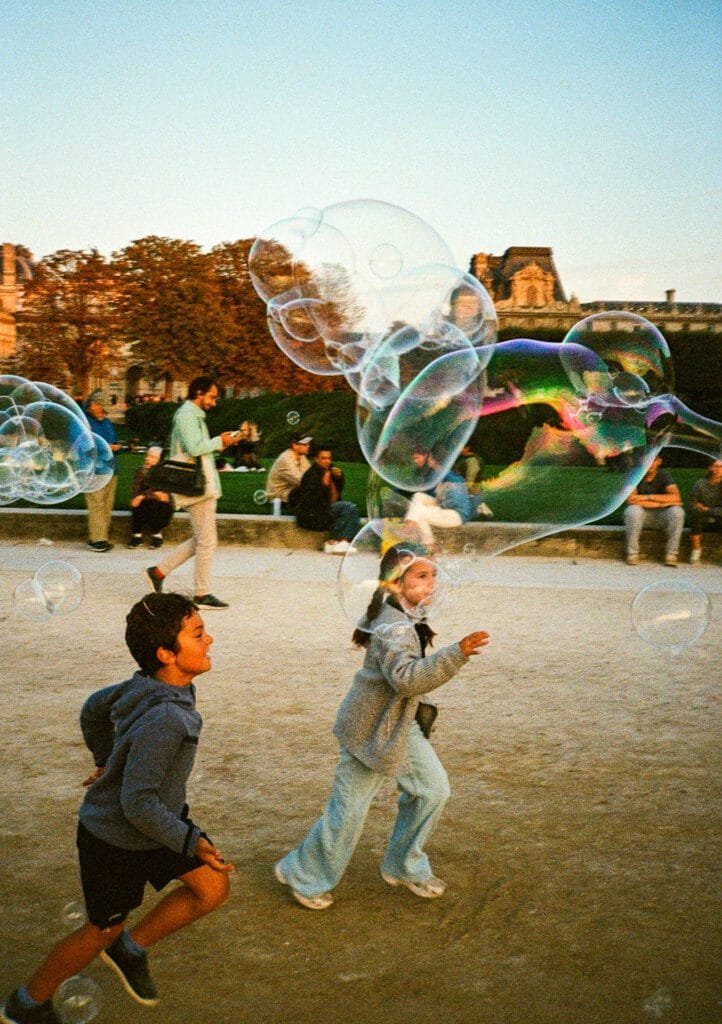 Deux enfants courant après des bulles de savon géantes au Jardin des Tuileries à Paris, photographiés sur pellicule Kodak Ultramax 400.