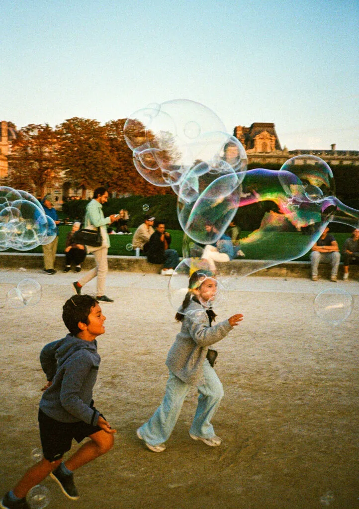 Deux enfants courant après des bulles de savon géantes au Jardin des Tuileries à Paris, photographiés sur pellicule Kodak Ultramax 400.