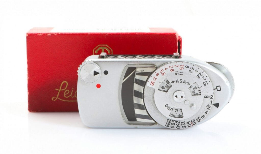 Leicameter MC avec molette d’exposition, affichage à aiguille et sa boîte rouge Leica d’origine, posé sur fond blanc.