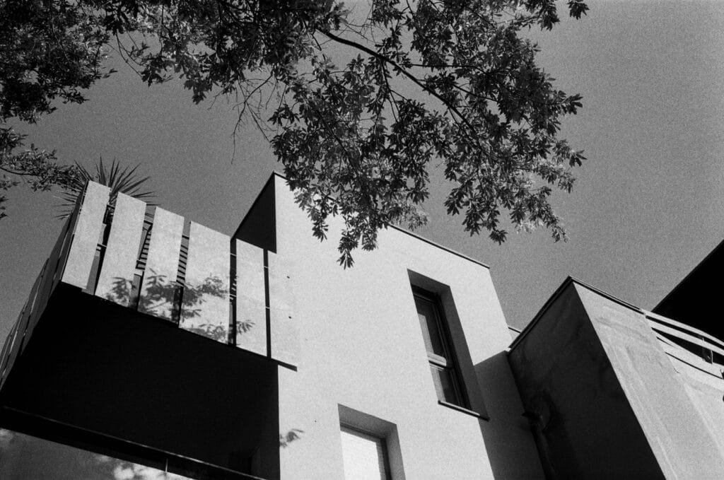 Façade d’un immeuble moderne et jeu d’ombres de feuillage en contre-plongée, capturés en noir et blanc dans le quartier des Olivettes à Nantes.