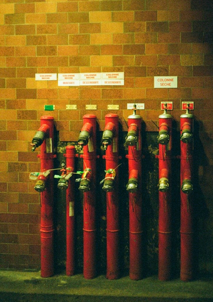 Rangée de colonnes sèches rouges sur fond de mur en briques, photographiée en lumière artificielle.