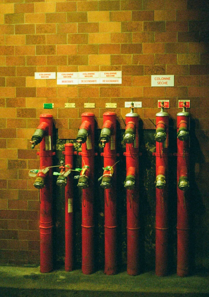 Rangée de colonnes sèches rouges sur fond de mur en briques, photographiée en lumière artificielle.