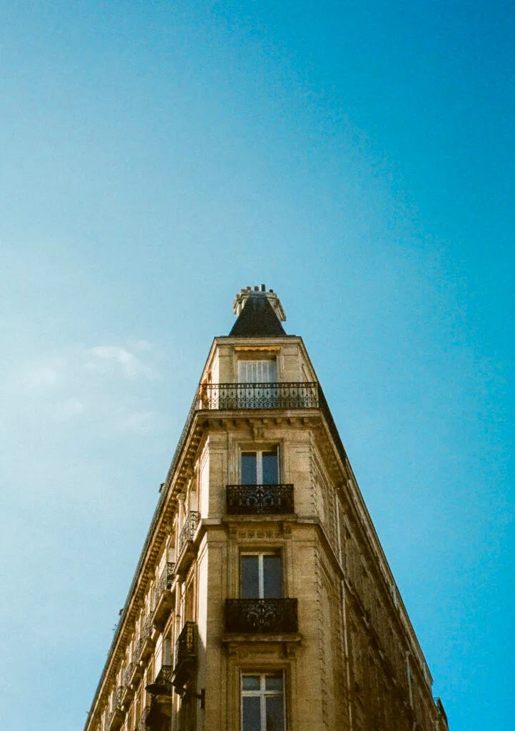 Immeuble haussmannien triangulaire photographié à Paris sous un ciel bleu, en demi-format.