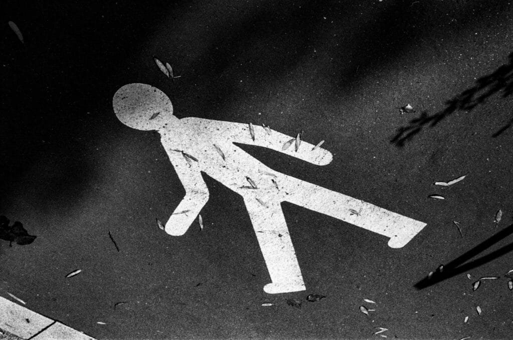 Silhouette peinte d’un piéton au sol, légèrement recouverte de feuilles mortes, photographiée en noir et blanc avec un fort contraste.