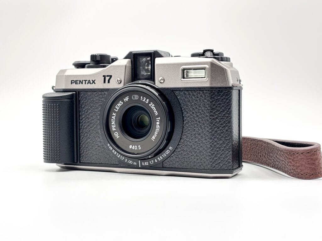 Appareil photo Pentax 17 posé sur fond blanc, vu de face avec son objectif 25mm f/3.5.